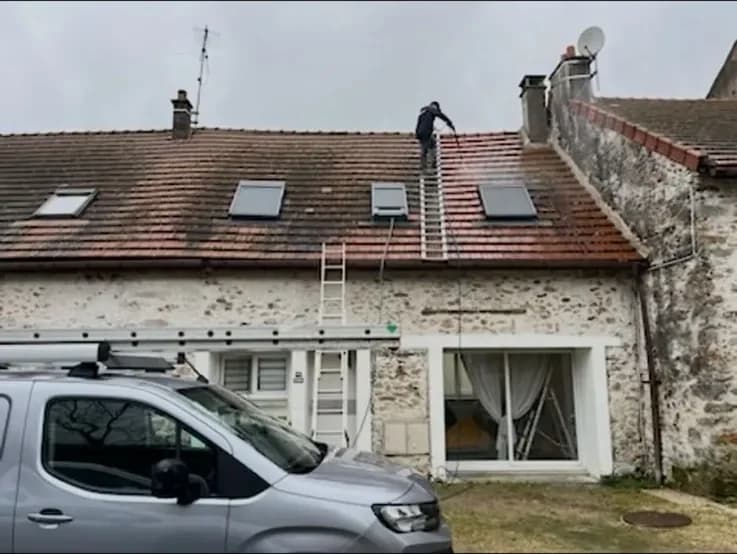 Une toiture en cours de nettoyage avec une échelle de couvreur posée sur les tuiles