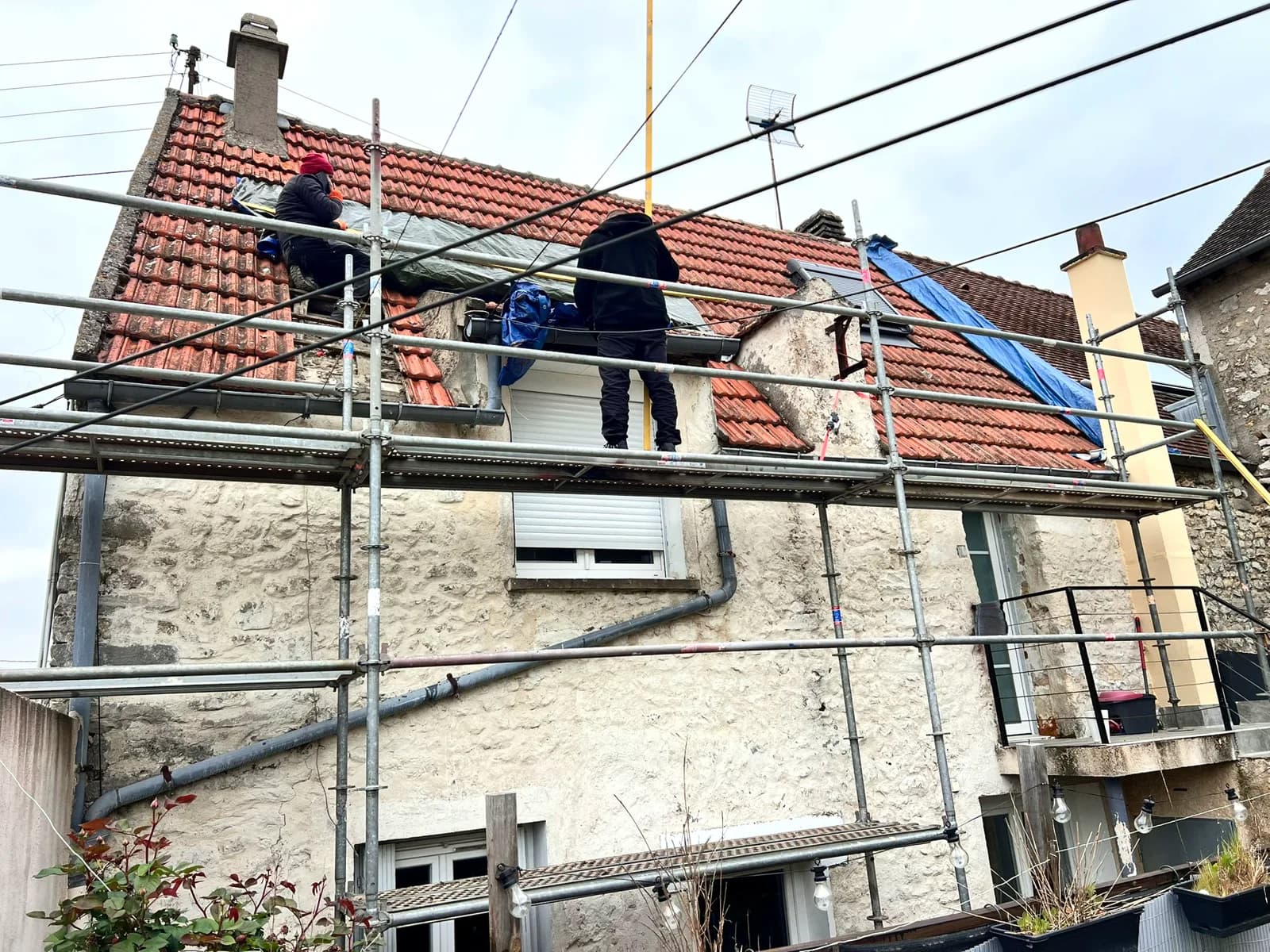 Une souche de cheminée en pierre sur une toiture ancienne, échafaudage en place