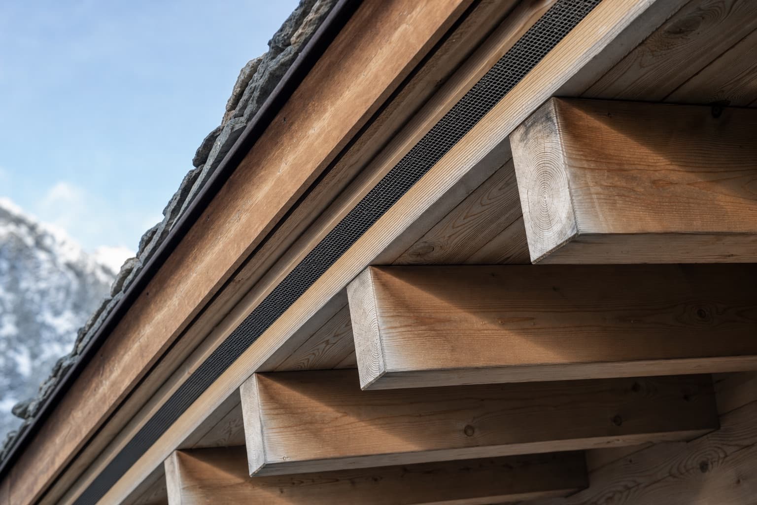 Illustration : le dessous d’un débord de toit alpin, chevrons de mélèze et lame d’air ventilée avec sa grille